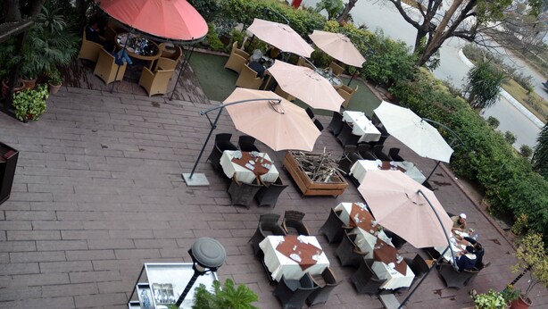 Eine Terrassengaststätte mit mehreren Tischen und Stühlen, von denen einige von Sonnenschirmen beschattet werden, und Kübelpflanzen rundherum.