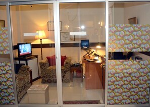 A living room with a sofa, a coffee table, a TV, and a laptop on a desk.