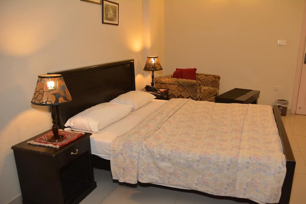 A neatly made bed with a floral bedspread, two bedside lamps, a nightstand, a small table with a red pillow, and a framed picture on the wall.