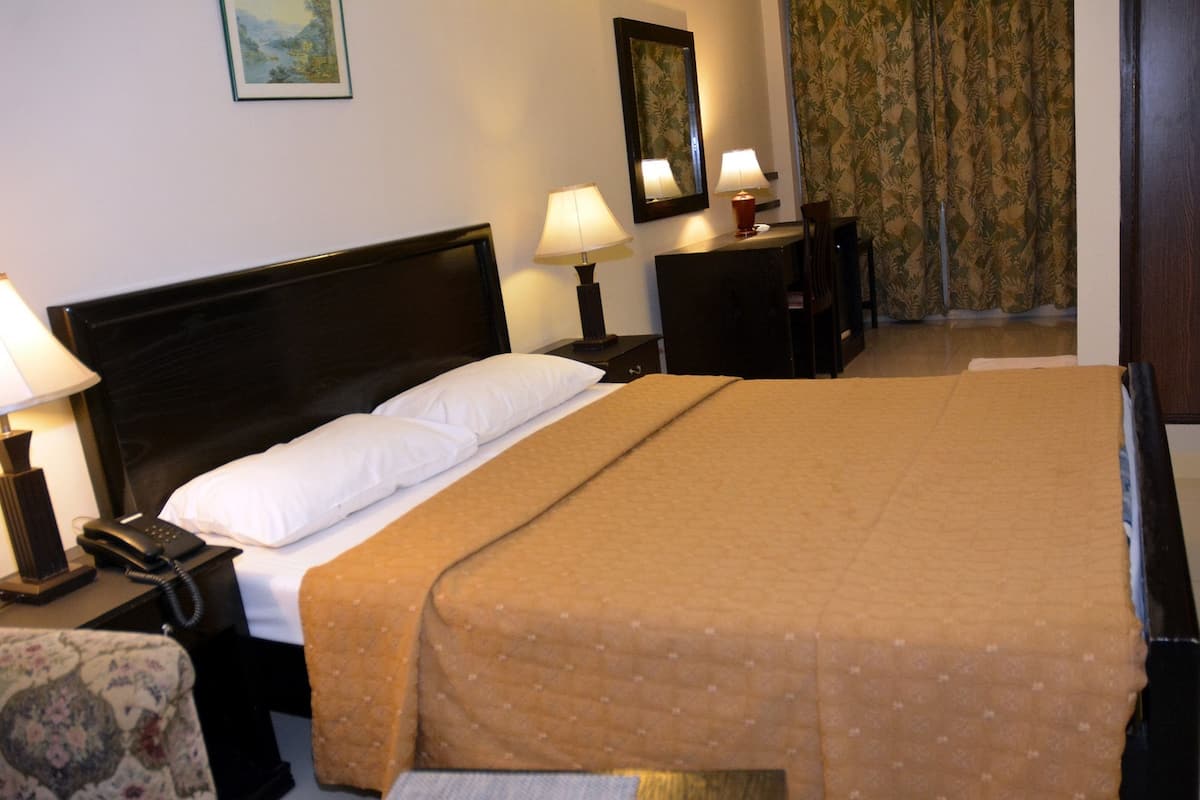 A hotel room with a large bed, two bedside lamps, a telephone, a small table, and a chair.