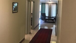 Ein Hotelkorridor mit rotem Teppich, einem gerahmten Bild an der Wand und Blick in einen Speiseraum mit Tisch und Stühlen.