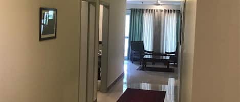 A hotel hallway with a red carpet, a framed picture on the wall, and a view into a dining area with a table and chairs.