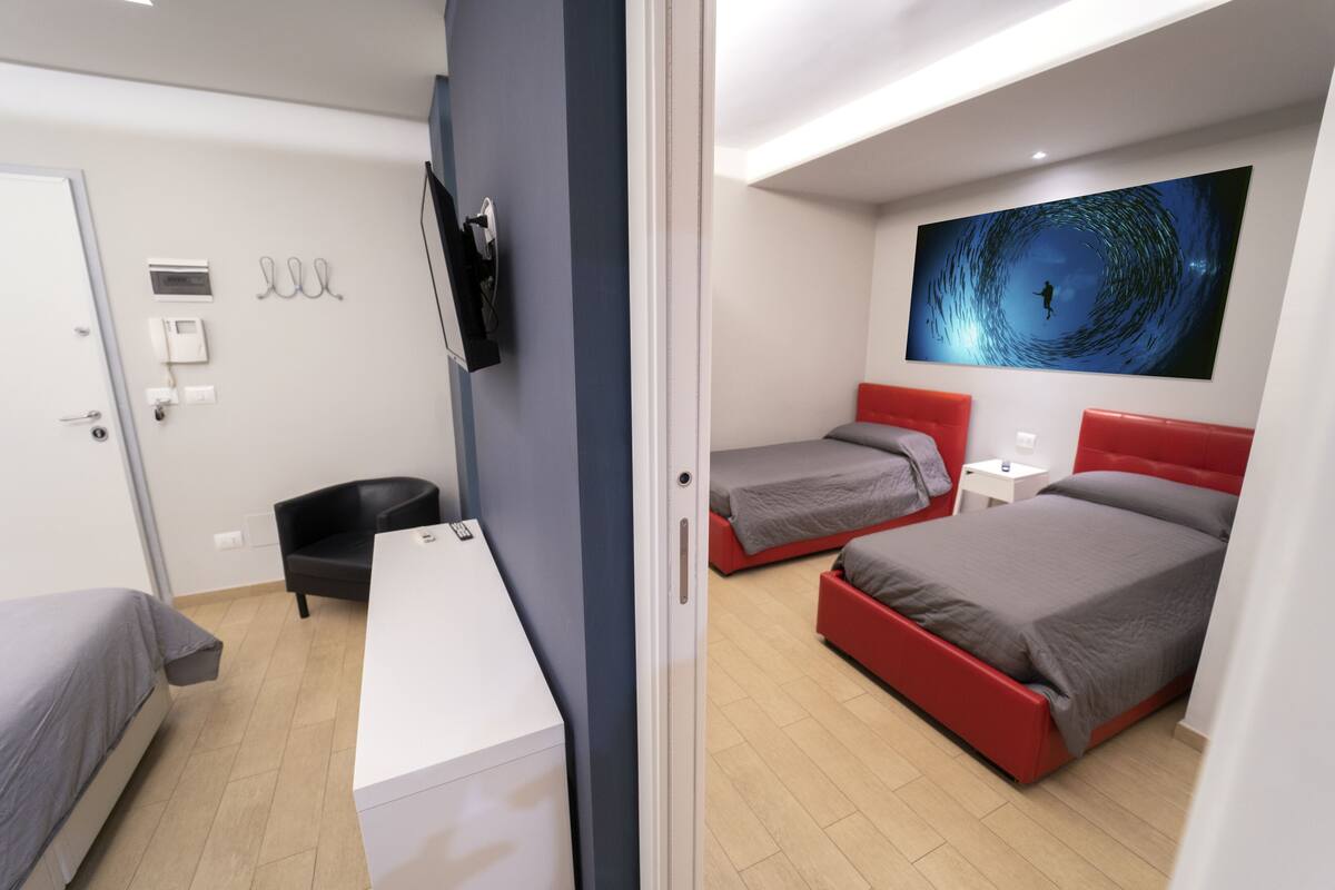 Une chambre d’hôtel moderne, équipée de deux lits, d’un bureau, d’une chaise, d’une télévision et ornée d’un grand tableau au mur.