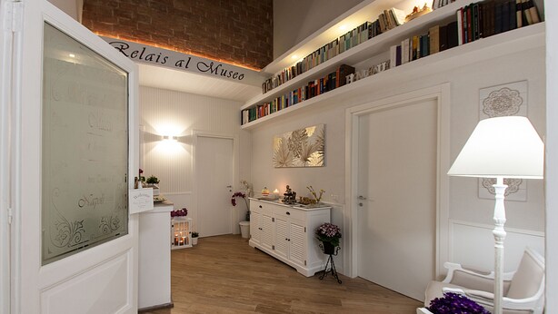A well-lit room with a wooden floor, a reception desk, a bookshelf, and a seating area with a lamp. - Relais al Museo (Naples)