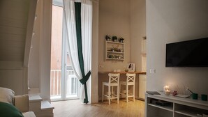 A living room with a sofa, a dining area with two chairs, a kitchen with a TV, and a balcony with curtains. - Relais al Museo (Naples)