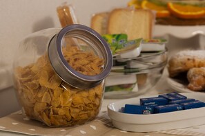 Lasipurkki täynnä muroja, lautanen, jossa on leipää, ja kulho, jossa on voinokareita.