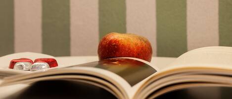 Un libro abierto con una manzana roja encima, y dos objetos rojos y plateados a la izquierda.