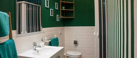 A bathroom with a white sink, a toilet, a shower with a glass door, and a green wall.