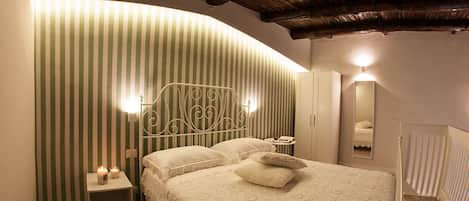 A bedroom with a curved ceiling, a bed with a patterned bedspread, a nightstand with candles, and a mirror on the wall.