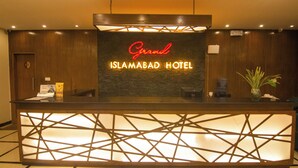 A reception desk with a sign reading "Grand Islamabad Hotel".