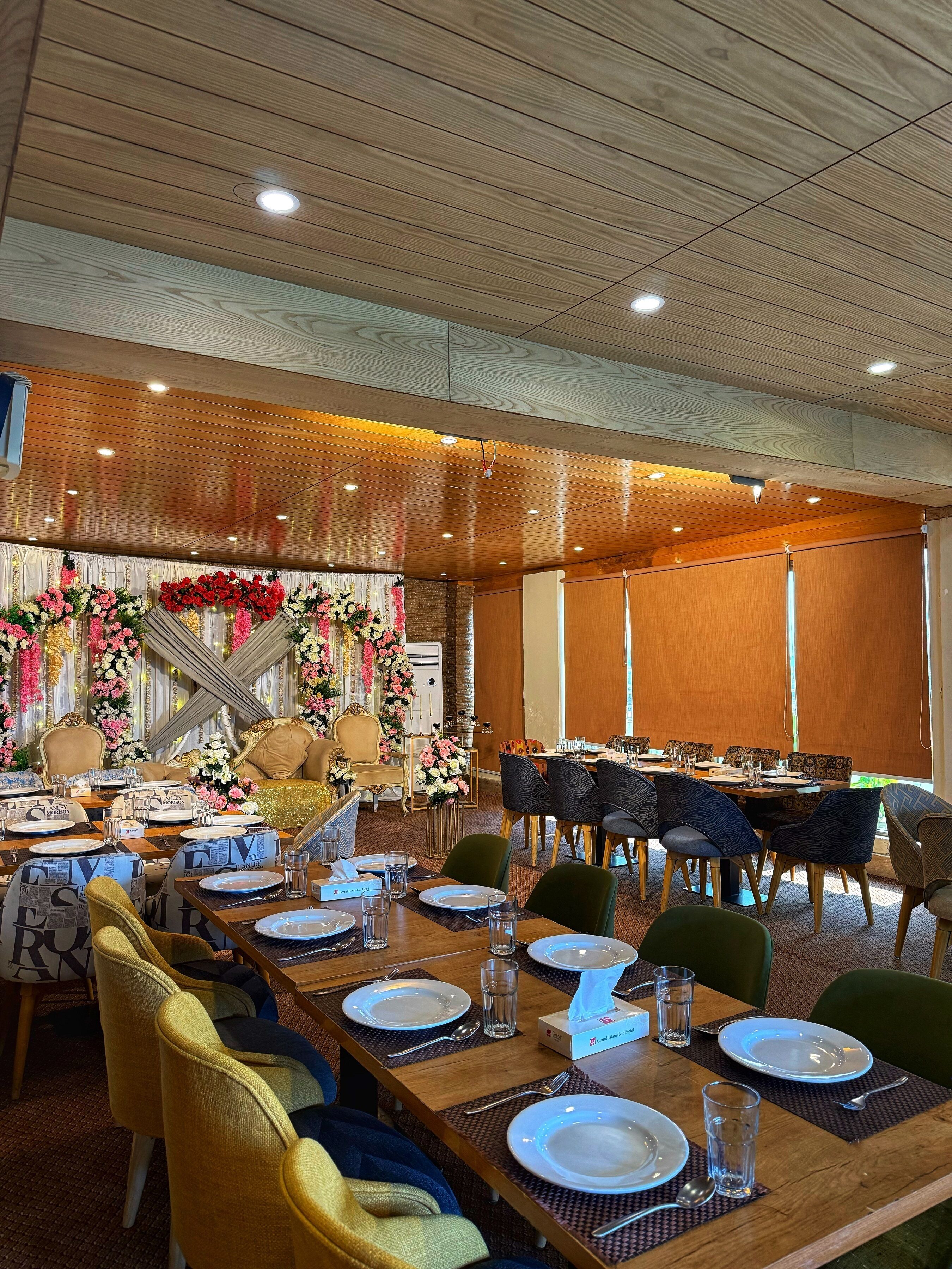 Een balzaal met houten lambrisering, bloemendecoraties en een lange tafel gedekt voor een maaltijd.