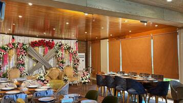 Een balzaal met houten lambrisering, bloemendecoraties en een lange tafel gedekt voor een maaltijd.