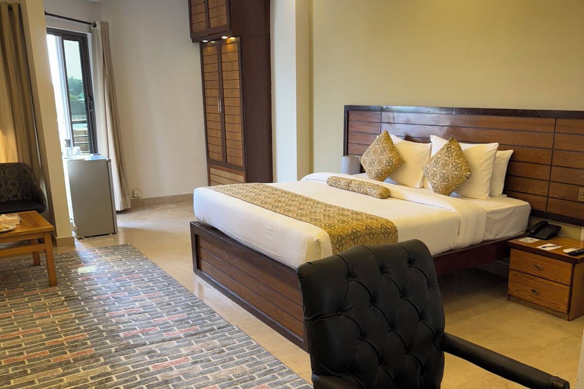 Een hotelkamer met een groot bed, een houten hoofdbord, een zwarte beklede stoel, een klein houten tafeltje en een vloerkleed met een baksteenmotief.