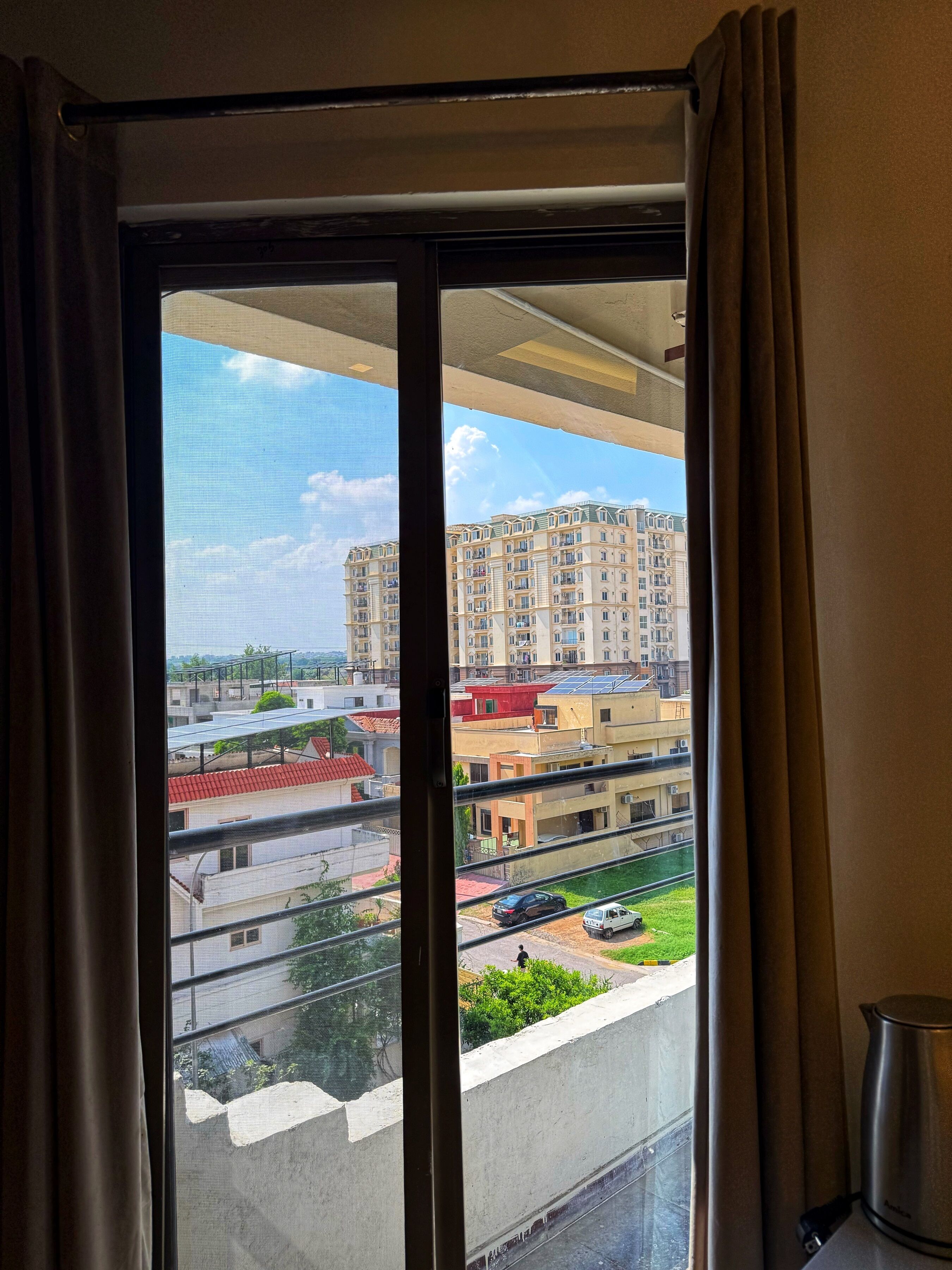 A view from a window with curtains, overlooking a residential area with multiple apartment buildings and a street below.