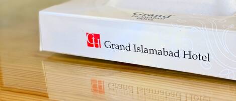 Paperipyyhekotelo, jonka päällä on Grand Islamabad -hotellin logo, ja se on asetettu puupinnalle.