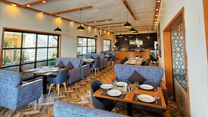 A modern restaurant with high ceilings, exposed wooden beams, and a herringbone wood floor. Tables are set with white plates and glasses, and there are blue upholstered seating areas.