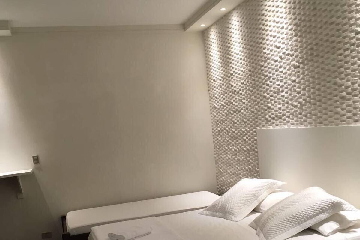 A bedroom with a bed, a ceiling fan, a textured wall, and a patterned rug.