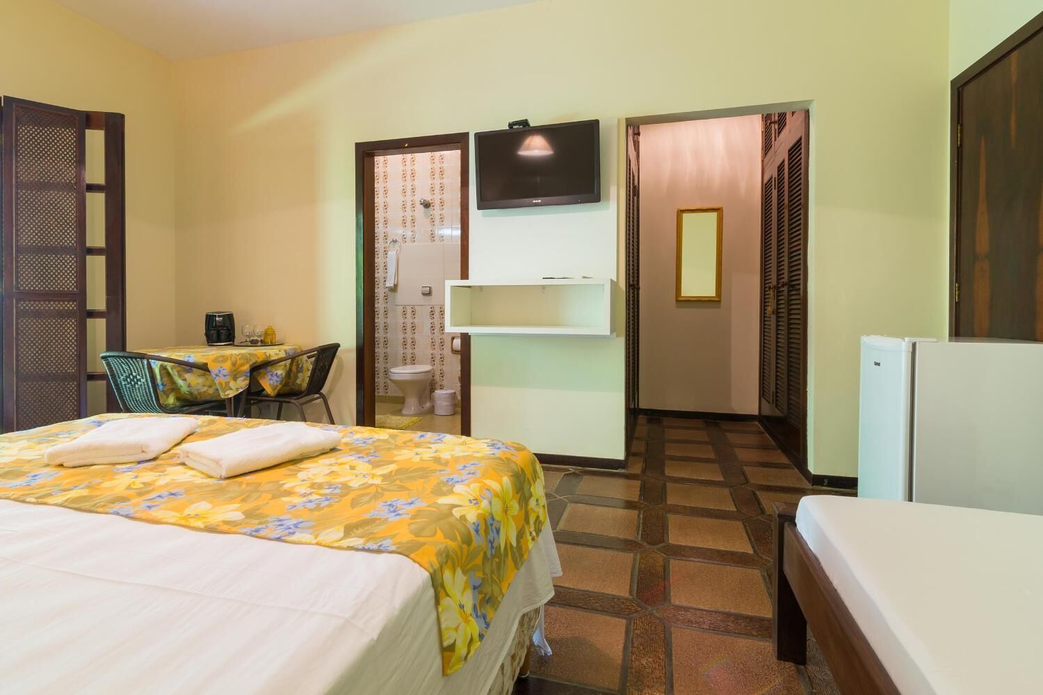 Ein Hotelzimmer mit einem Bett, einem kleinen Tisch mit Stuhl, einem Fernseher und einem Kühlschrank.