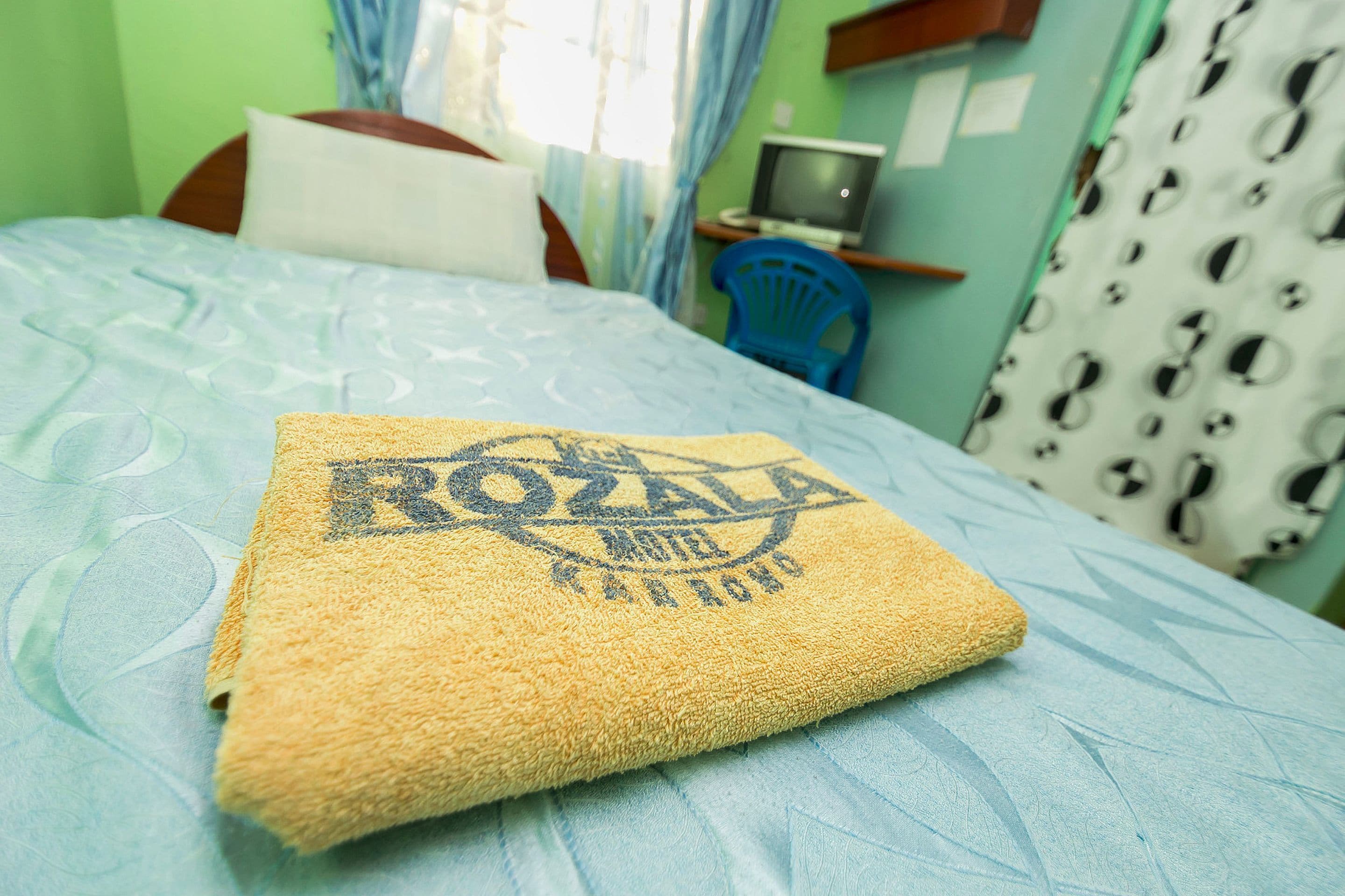 Een bed met een blauw beddekleed met patroon, een gele handdoek met een logo, en een televisie op een standaard op de achtergrond.