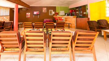 A restaurant with wooden chairs and tables, a counter, and a TV on the wall.