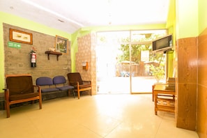 A reception area with a fire exit sign, a fire extinguisher, a wooden bench, a television, and a glass door leading outside.