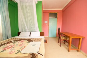 A room with a bed, a wooden table, and a chair. There is a door in the background.