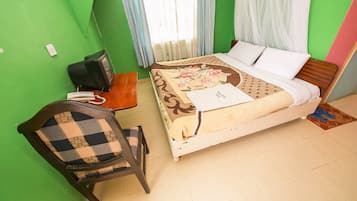 Una habitación con cama, una silla, escritorio con teléfono y ventana con cortinas.