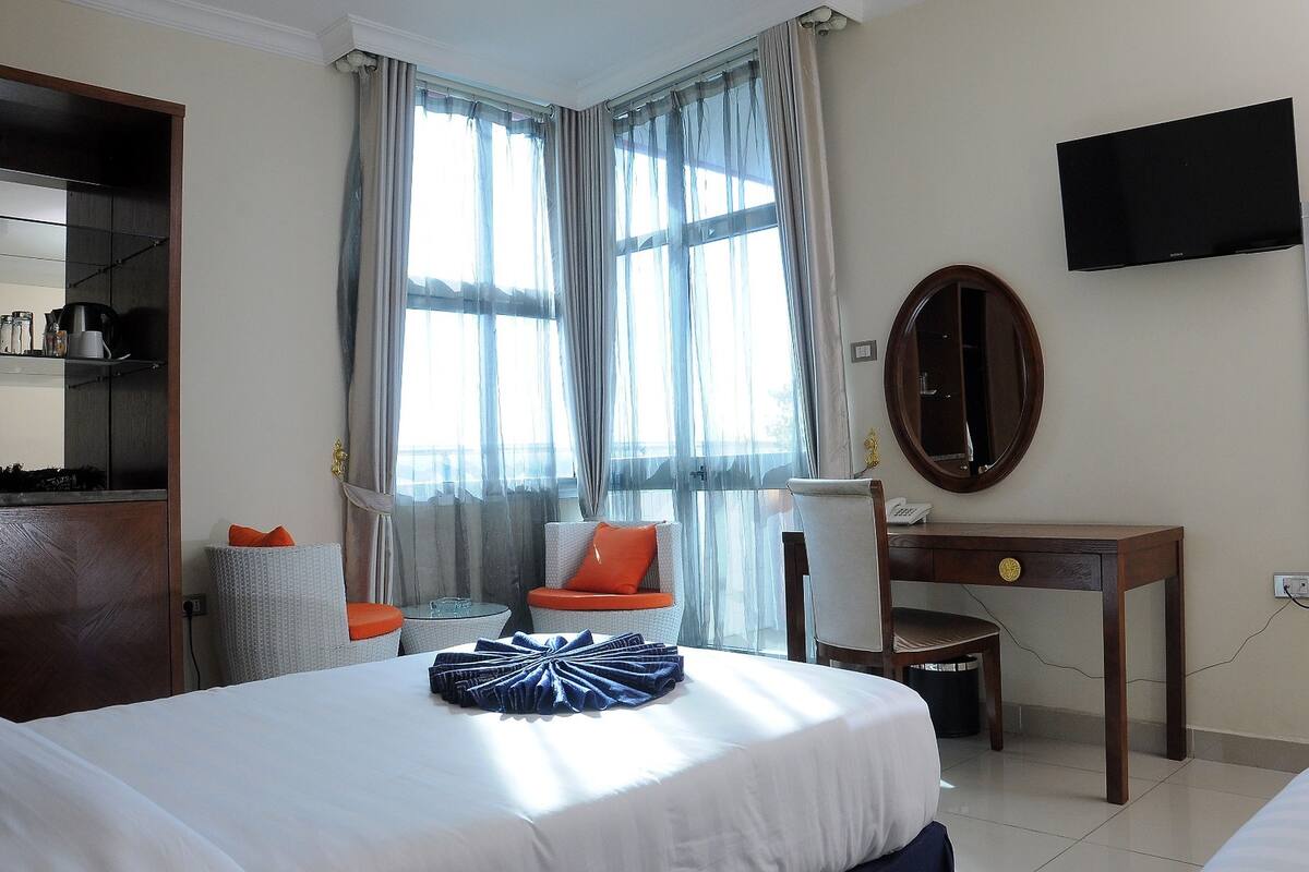 A hotel room with a bed, a desk, a chair, a television, and a large window with curtains.