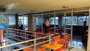 Restaurante com cadeiras e mesas laranja, guarda-corpo de vidro e vista para o exterior.