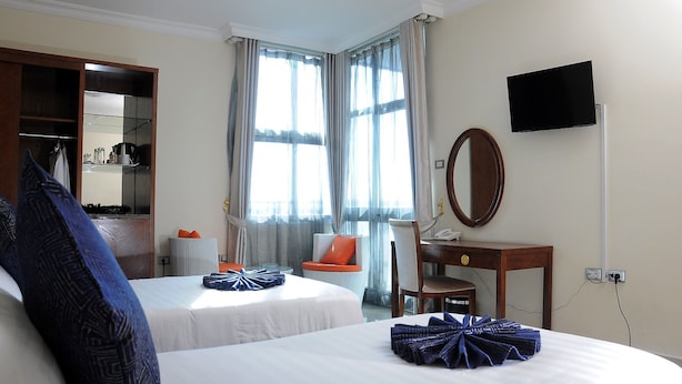 Quarto de hotel com duas camas, uma escrivaninha, uma cadeira, uma televisão e um guarda-roupa.