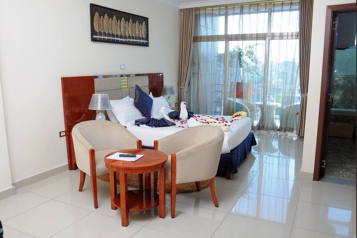 A hotel room with a bed, two chairs, a small table, and a window with curtains.