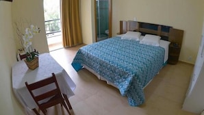Habitación de hotel con cama, una mesa y una silla, balcón con cortinas y una ventana.