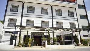 Un edificio de varios pisos con balcones, un acceso cubierto y plantas en macetas.
