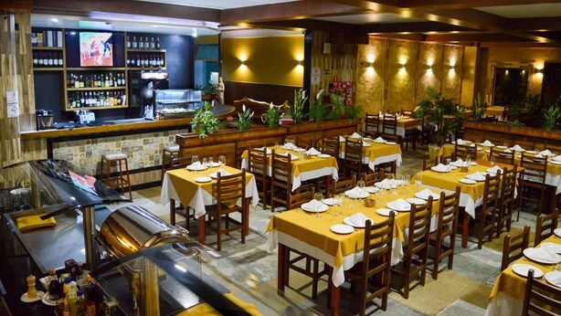 Un restaurante con varias mesas dispuestas para comer, una zona de bar con diversidad de botellas y un mostrador con una pantalla de televisión.