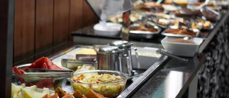 Un bufé con diversas frutas y platos, incluyendo sandía, manzanas y un bol de ensalada de frutas mixtas.
