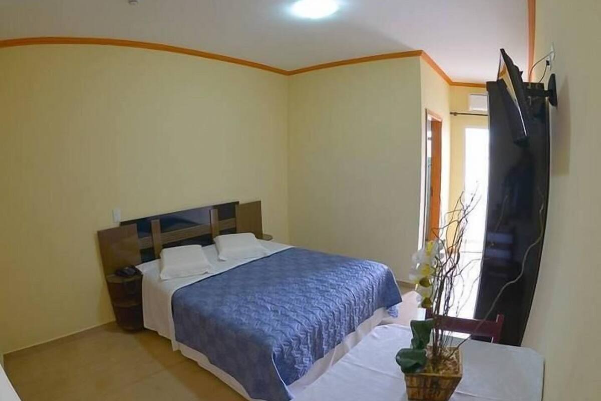 A bedroom with a bed, bedside table, and a potted plant.