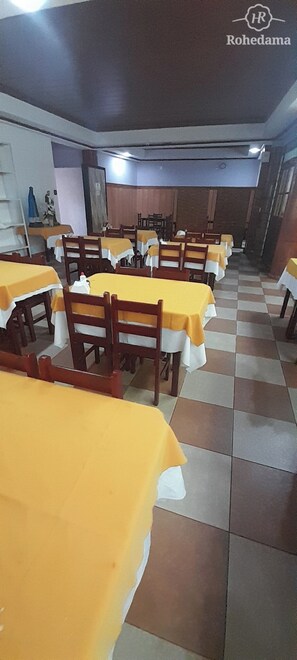 Un espace repas avec plusieurs tables recouvertes de nappes jaunes, des chaises en bois et un motif de sol à carreaux.