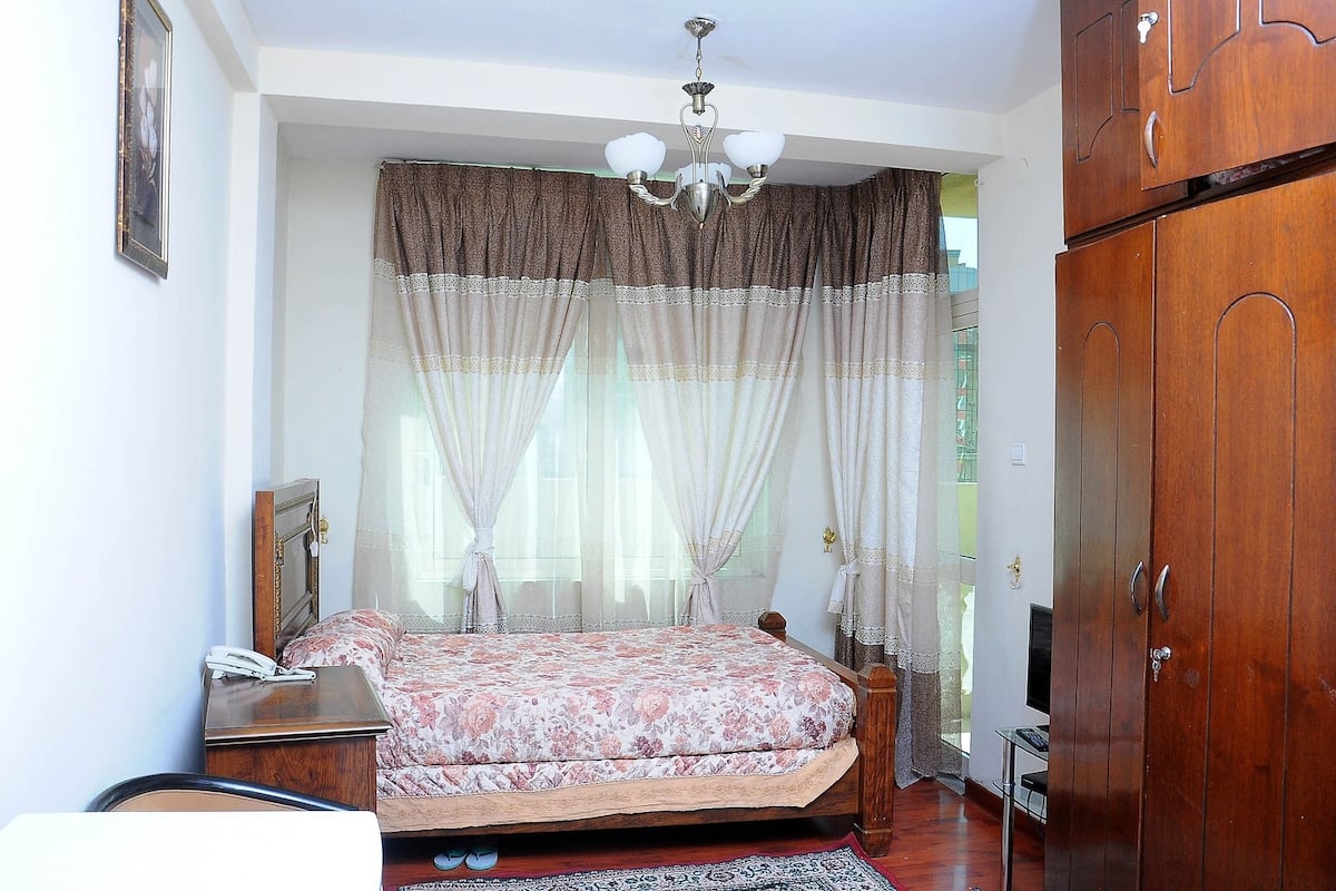 Une chambre à coucher avec un lit, une table de chevet avec un téléphone, une armoire en bois et un lustre.