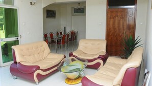 A living room with two beige and red sofas, a glass coffee table, and a dining area with red chairs and a wooden door. - Grand Guest House (Addis Ababa)