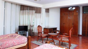 A hotel room with a bed, a TV, a dining table with chairs, and a wardrobe. - Grand Guest House (Addis Ababa)
