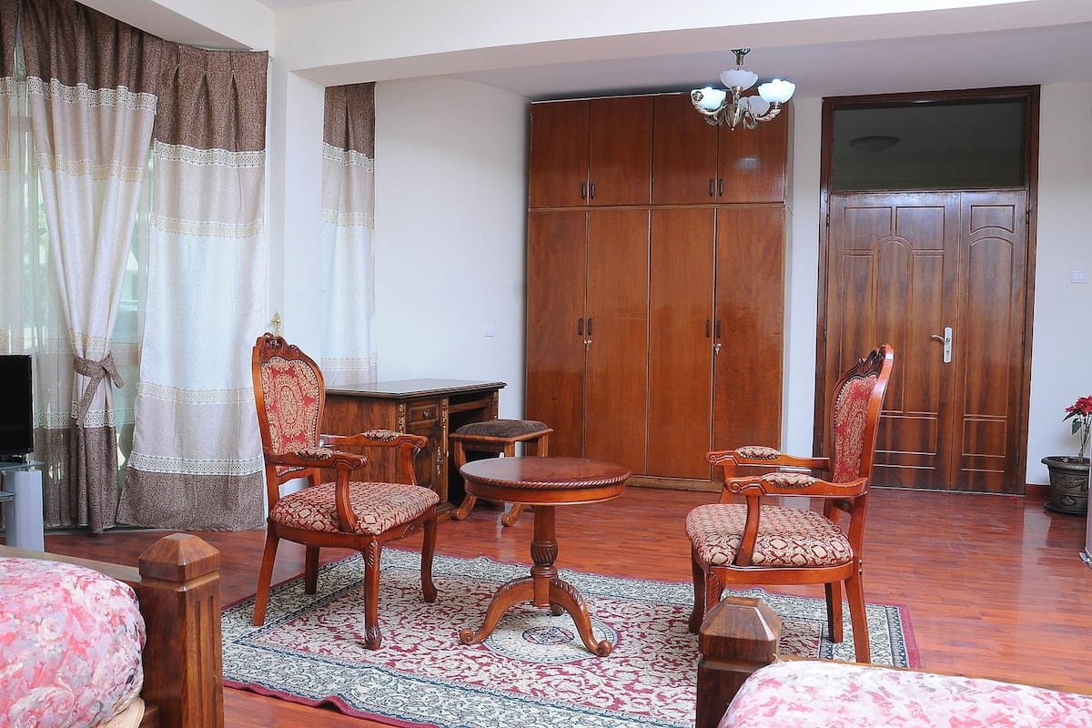 Une pièce comprenant un lit, deux chaises en bois, une petite table ronde, une armoire et un téléviseur.