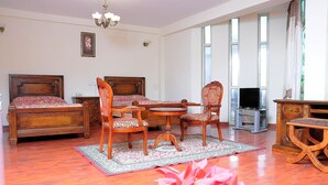 A room with two wooden beds, a dining table with chairs, a TV, and a large window with curtains. - Grand Guest House (Addis Ababa)