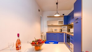 A modern kitchen with blue cabinets, a white countertop, and a fruit bowl with grapes and strawberries. - Desenzanoloft – Desenzano Corte Blu Downtown (Desenzano del Garda)