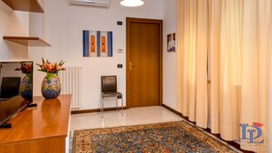 A hotel lobby with a reception desk, two vases with flowers, a chair, a door, a radiator, a patterned rug, and a hanging light fixture. - Desenzanoloft – Desenzano Corte Blu Downtown (Desenzano del Garda)
