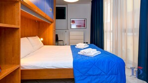 A hotel room with a bed, a blue bedspread, and a wooden wardrobe. - Desenzanoloft – Desenzano Corte Blu Downtown (Desenzano del Garda)