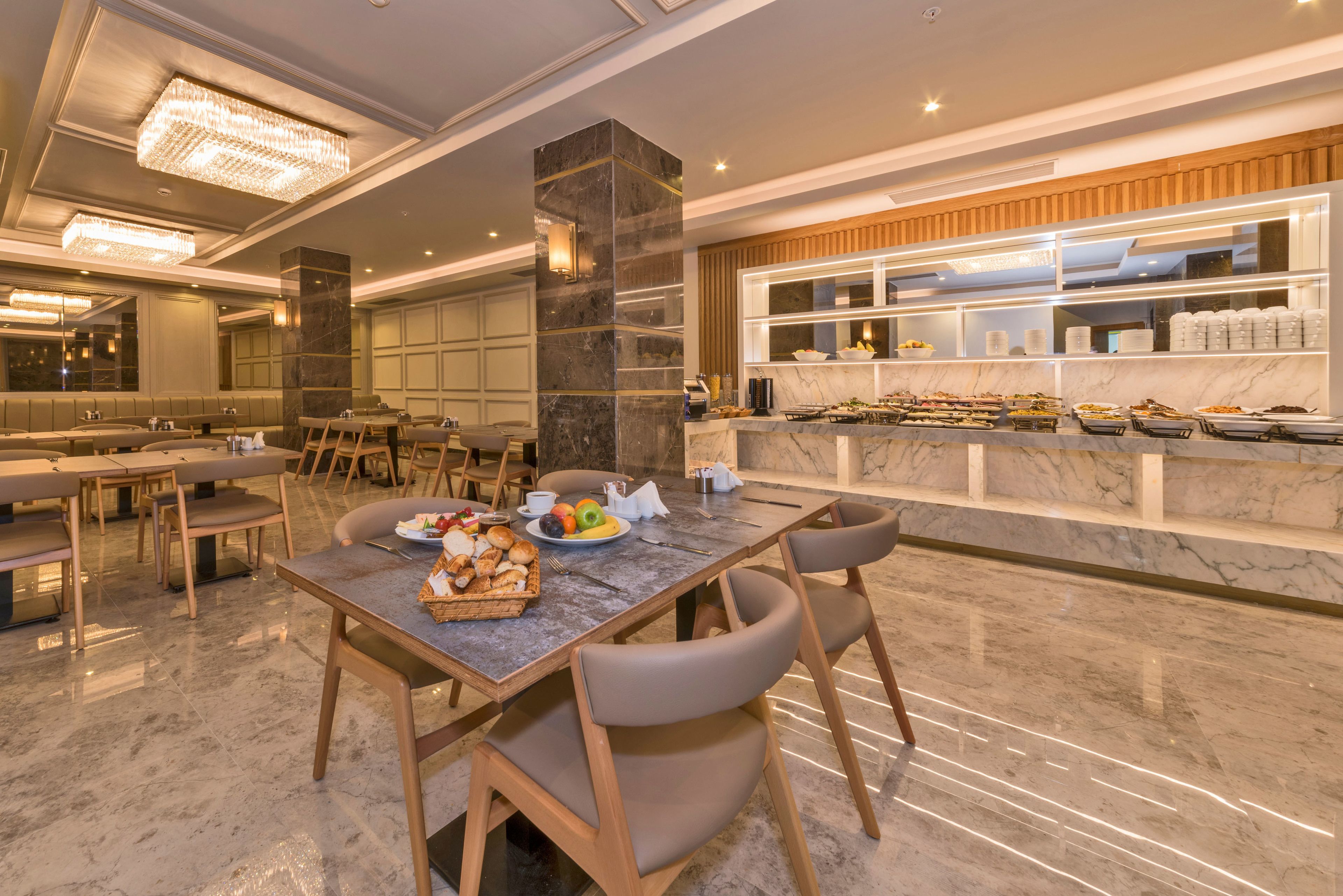 A spacious dining area with marble flooring, modern lighting, and a buffet counter with various food items.