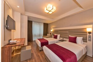 Una habitación de hotel con dos camas, un escritorio con televisor y una lámpara moderna.