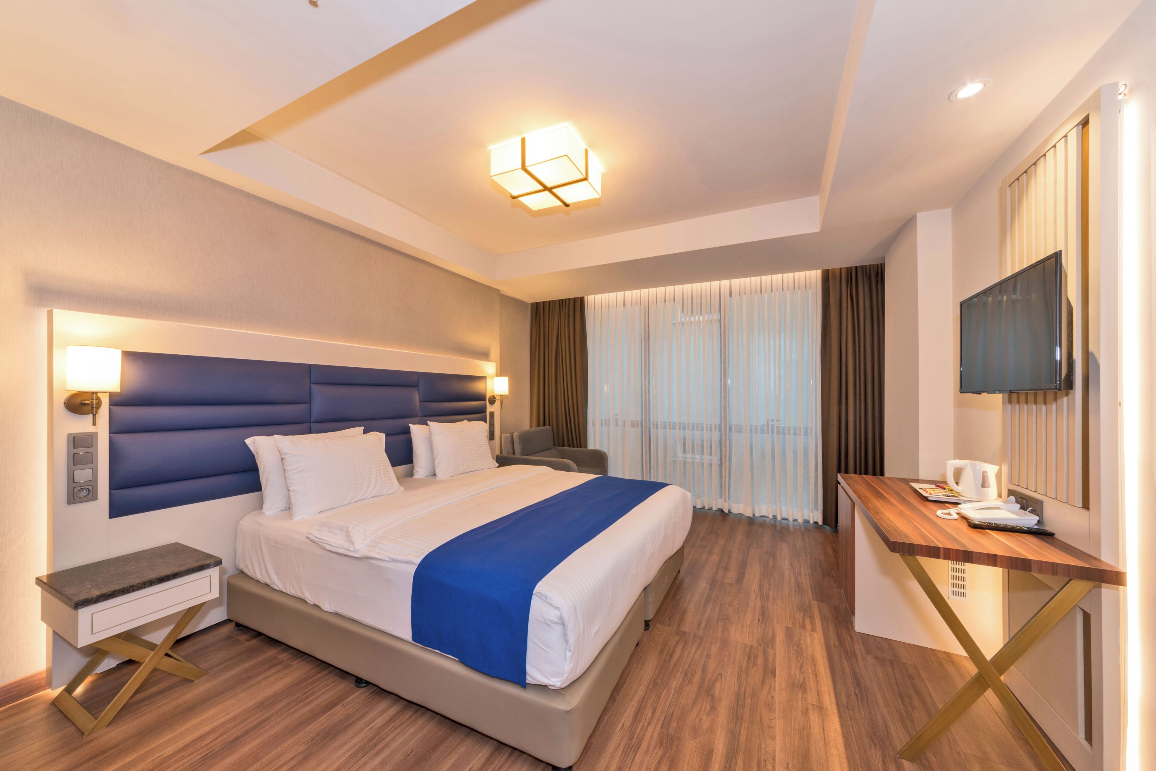 A hotel room with a bed, bedside table, desk, and a TV.