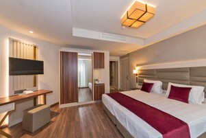 A modern hotel room with a large bed, a desk, a television, and a mirror.