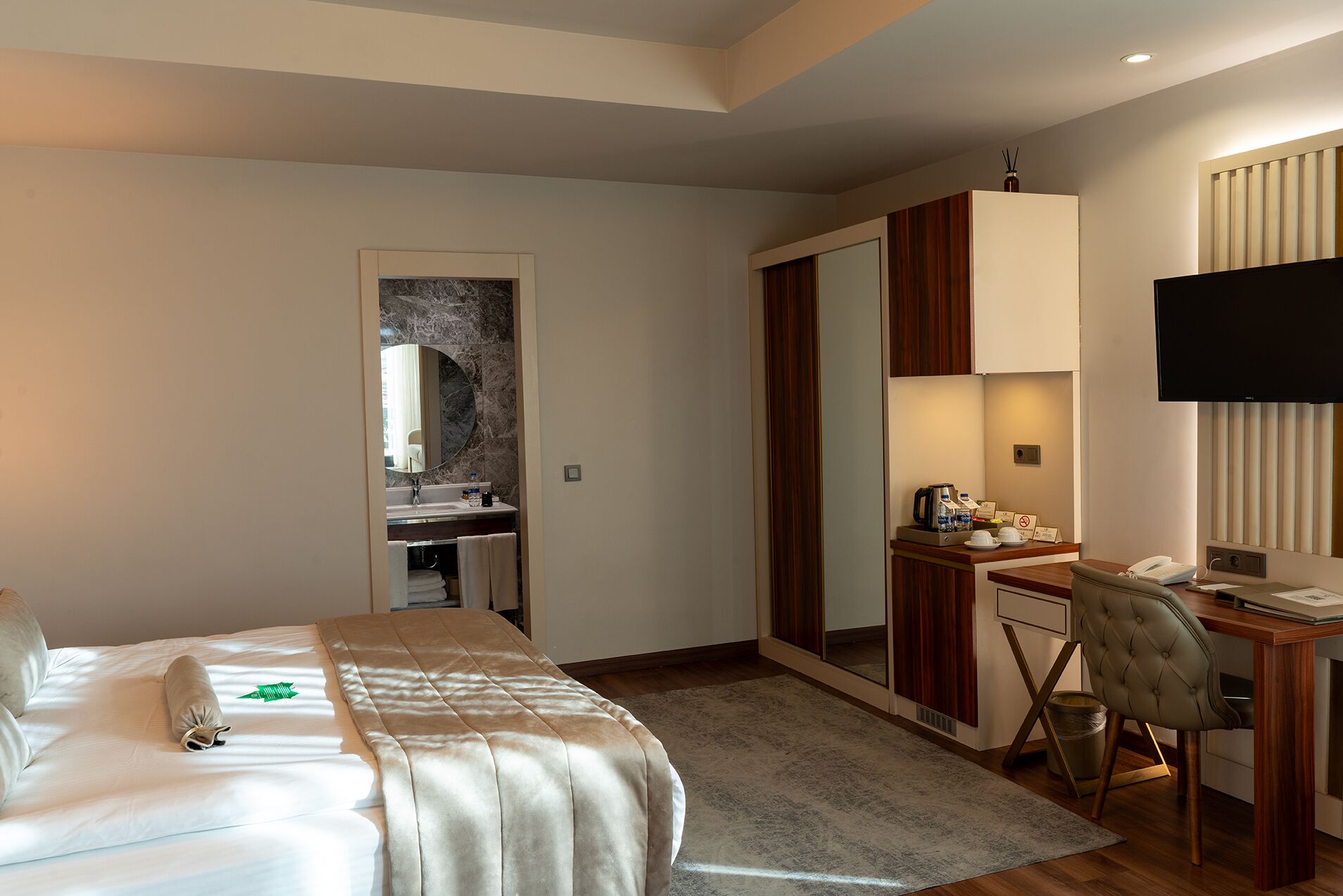Una camera d'albergo con un letto, una scrivania, una sedia, una televisione e un bagno.